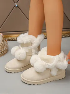 Close-up detail of cozy beige snow boots featuring cute pom-poms and warm plush lining.
