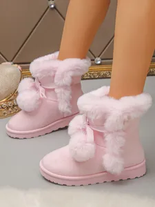 Detailed view of pink plush snow boots with cute bow and pom-poms, thick warm winter footwear.