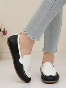 Nahaufnahme von schwarz-weißen Damen-Slippern in flacher Ausführung mit Ziernähten.
