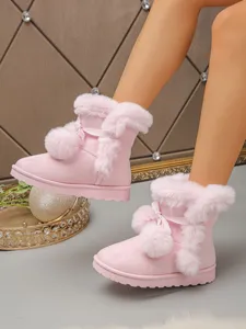 Pink furry snow boots detail showing cozy plush lining, cute pom-poms and bow decoration.