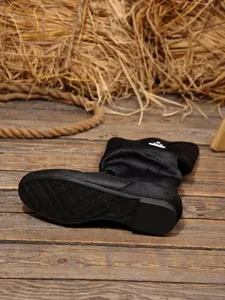 Λεπτομερής λήψη μαύρης slouchy μπότας με ανάγλυφη σόλα πάνω σε ρουστίκ ξύλο.