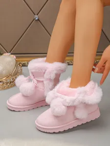 Close-up view of cozy pink winter snow boots featuring cute plush pom-poms and thick soles.