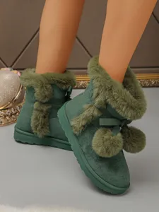 Close-up detail of green fuzzy snow boots with cute bow and pom-pom decor, thick sole.