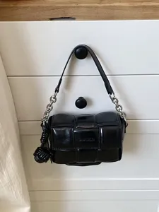 Sac bandoulière tissé noir avec bandoulière en chaîne métallique et design en cuir matelassé pour femmes.