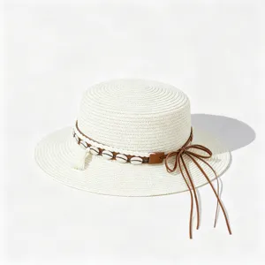Detail of stylish flat top straw hat with leather strap, seashells and tassel for summer sun.