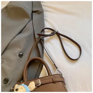 Brown leather handbag detail shot featuring top handle, adjustable strap and cute bear charm.