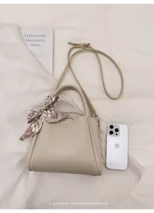 Detailansicht einer minimalistischen beigen Ledertasche mit Schal und Schultergurt.