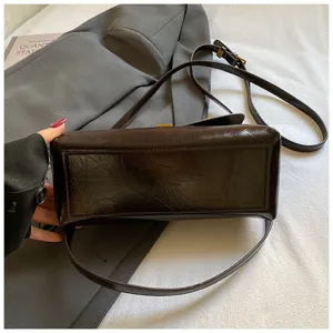 Glossy dark brown shoulder bag detail view, showing vintage texture and metallic clasp.