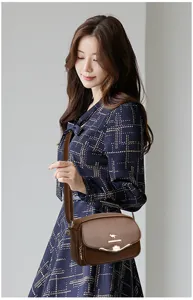 Detail view of brown PU leather shoulder bag worn by model, showing metal logo accent.