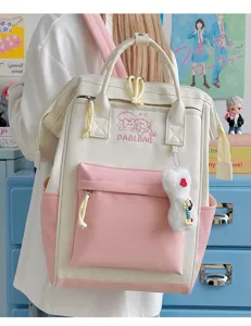 Nahaufnahme des süßen Kontrast-Canvas-Rucksacks mit Plüschanhänger und zarter Stickerei.