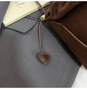 Detailed shot of a stylish brown suede bucket bag with a cute heart charm drawstring design.