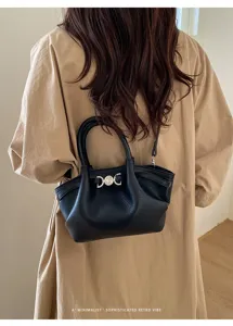 Detailed shot of black leather shoulder bag with metal heart clasp worn by model in trench coat.