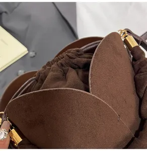 Close-up detail of dark brown suede bucket bag showing petal flap and golden hardware.