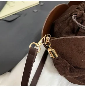 Close-up detail of brown suede bucket bag featuring elegant gold hardware and drawstring.