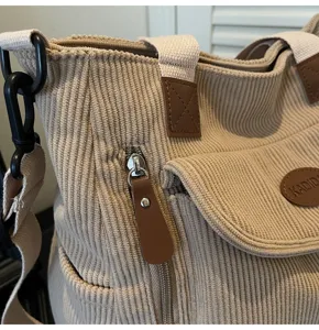 Close-up of beige corduroy shoulder bag showing zipper pocket and fabric texture.