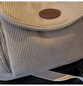 Close-up of casual khaki corduroy shoulder bag texture detail with stylish brand logo patch.