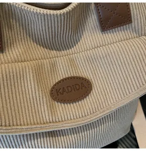 Close-up detail of beige corduroy tote bag showing textured fabric and brown leather label.