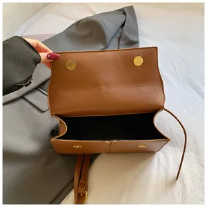 Détail intérieur de sac à main structuré marron avec boutons aimantés dorés et bandoulière.