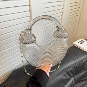 Clear acrylic knot handbag with gold chain strap, stylish transparent crescent design detail.