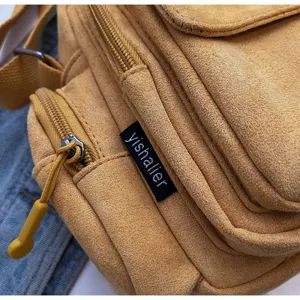 Close-up detail view of yellow suede camera shoulder bag zipper and brand label craftsmanship.