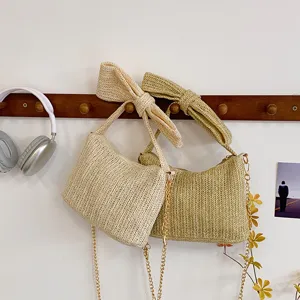 Strohgewebte Umhängetasche mit Schleife und eleganter Metallkette für sommerliche Damenmode.