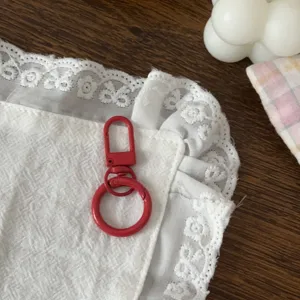 Primo piano dettagliato del portachiavi con anello a molla rosso su tessuto di pizzo bianco.