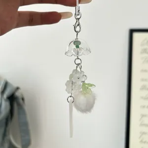 Clear detail shot of a minimalist translucent bell and flower phone charm, cute bag accessory keychain.