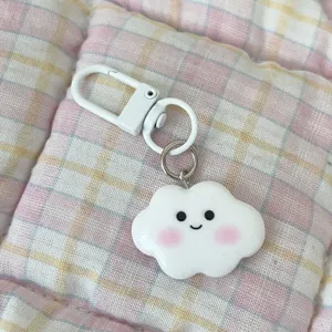 Cute white cloud keychain with pink blush and smiling face pendant on plaid background.
