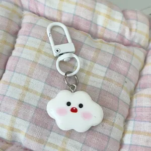 Close-up detail shot of a cute white cloud keychain with smiling face and pink blush design.