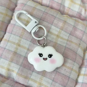Close-up detail of a cute white cloud keychain with smiling face and pink blush cheeks.