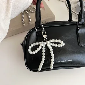Chic borsa a mano nera con elegante ciondolo a fiocco di perle per un look alla moda.