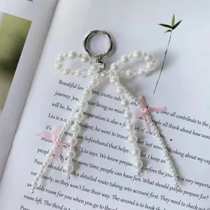 Pearl bow keychain detail, elegant white pearls with pink ribbon and metal ring, flat lay.
