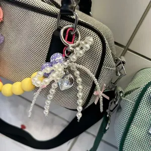 Close-up detail of trendy pearl bow bag charm keychain with colorful beads and heart pendant.