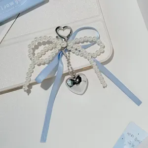 Close-up detail of a charming pearl bow keychain with a cute blue ribbon and silver heart charm.