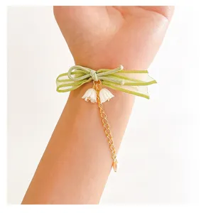 Dettaglio elastico fiocco fiore verde, nastro trasparente e graziosi ciondoli mughetto.