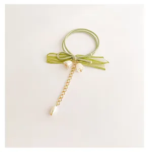 Vista dettagliata dell'elastico per capelli con fiocco mughetto verde, catenina e perle.
