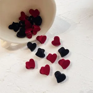 Primo piano di mini mollette per capelli a cuore in velluto nero e rosso da una tazza bianca.