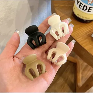 Close-up detail shot of four matte mini hair claw clips in assorted colors held in hand.
