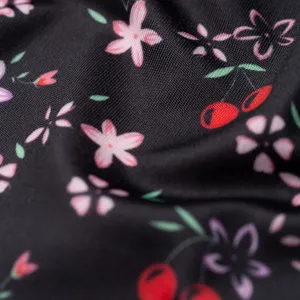 Close-up detail of smooth black ice silk fabric featuring cute pink floral and red cherry prints.