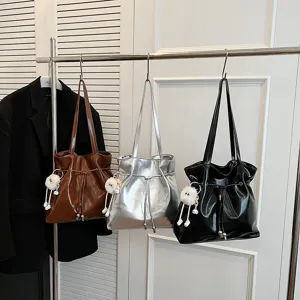 Detailaufnahme glänzender PU-Leder Schultertaschen am Ständer mit niedlichen Anhängern.
