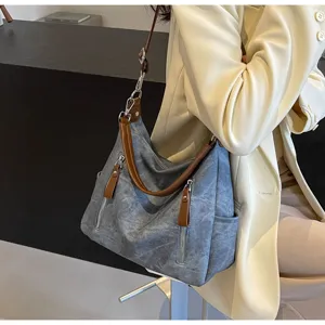 Nahaufnahme der stylischen, grauen Schultertasche mit braunen Ledergriffen und Reißverschlüssen.