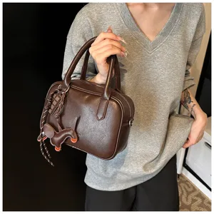 Detailansicht der braunen Retro Boston Handtasche aus Leder mit Griffen und süßen Anhängern.