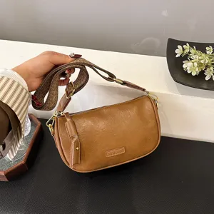 Braune Leder Umhängetasche Detail zeigt Schulterriemen, Metallbeschläge und Markenlogo.