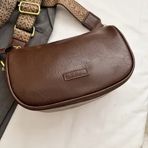 Nahaufnahme einer dunkelbraunen PU-Ledertasche mit breitem Ethno-Gurt und goldenen Beschlägen.