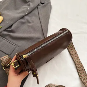 Nahaufnahme einer braunen Zylindertasche mit breitem, gemustertem Gurt und Metallreißverschluss.