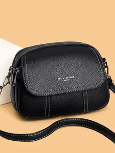 Nahaufnahme einer schwarzen Leder-Minicrossbody-Tasche mit Kontrastnähten und Reißverschlüssen.