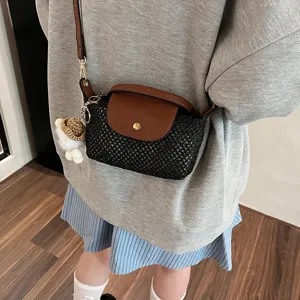 Detailaufnahme der schwarzen geflochtenen Umhängetasche mit brauner Klappe und Anhänger.