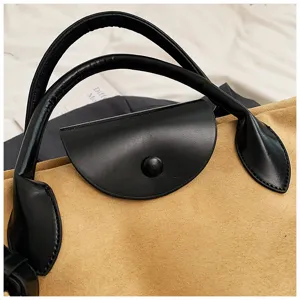 Detailaufnahme einer stilvollen Wildleder Tasche mit schwarzem Ledergriff und Überschlag.