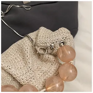 Detailaufnahme einer Sommer-Strohtasche mit großen rosa Perlen und glänzender Metallschließe.