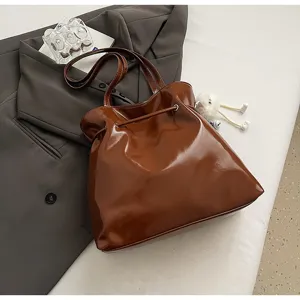 Detailaufnahme der braunen Lackleder Schultertasche mit Kordelzugverschluss und eleganten Riemen.